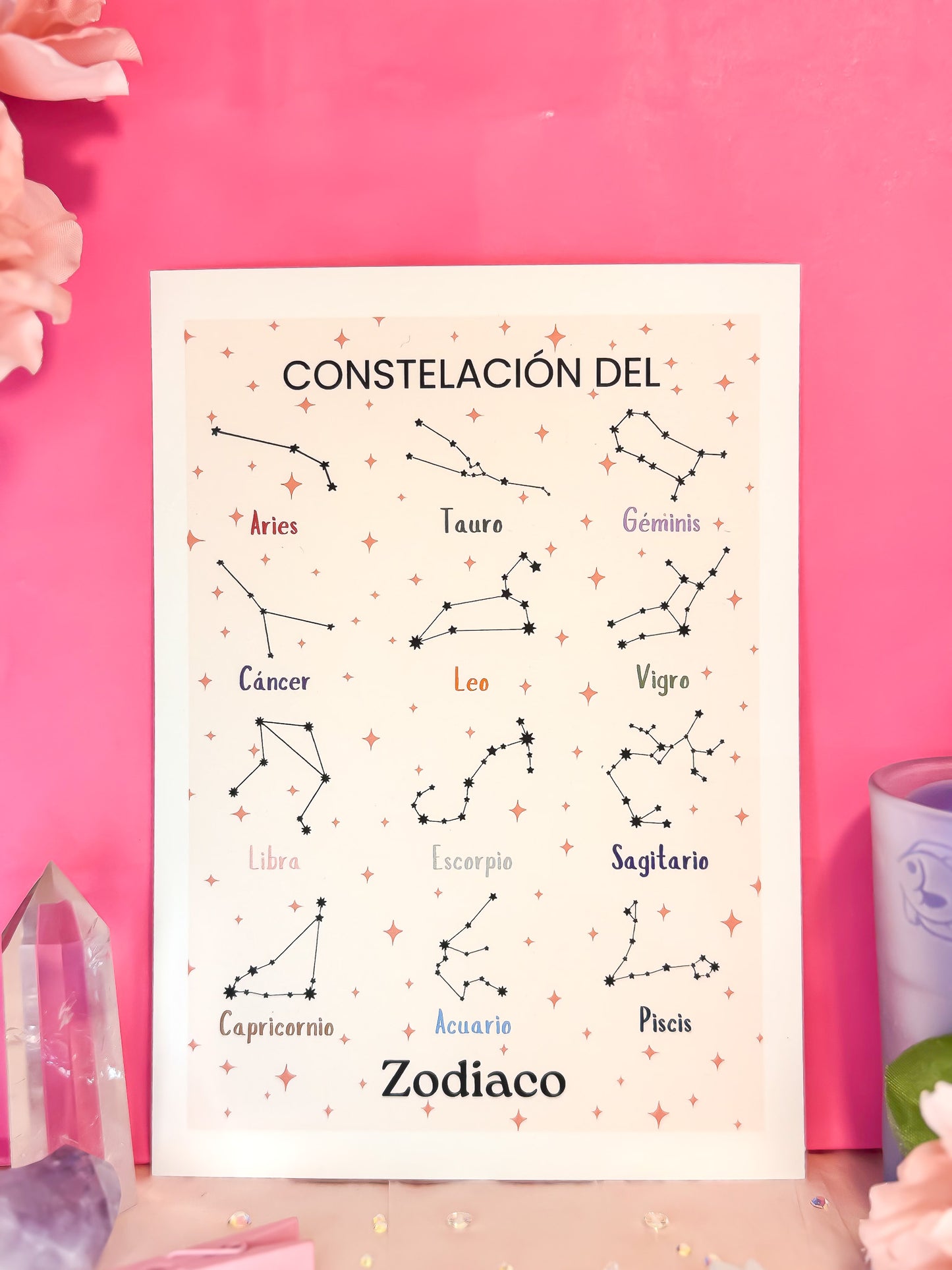 Spanish zodiac print with constellations of all 12 signs on a light background styled against a vibrant pink background with crystals and flowers by Cosmic Charms.